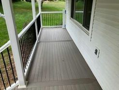 Gray deck with black railing and white columns, attached to a white house with a window.