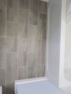 Gray wood-look tile on a bathroom wall next to a white tub and wall.