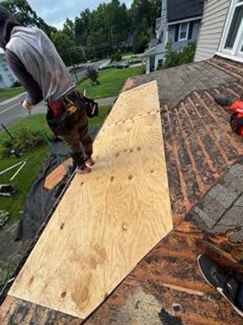 A person on a rooftop installing plywood. The roof is old and damaged.