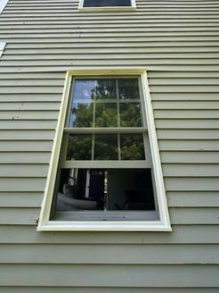 Exterior view of a window on a light green clapboard house. The window is white-framed and has a nine-pane grid.