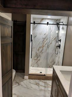Bathroom with marble shower and floors, sliding glass door, dark wood accents.