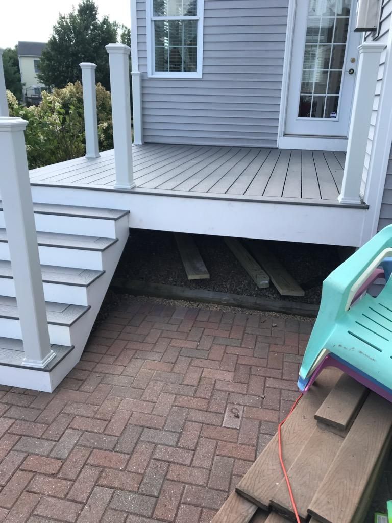 Exterior view of a deck with stairs, a door, and a brick patio. A child's chair and wood pieces are on the patio.
