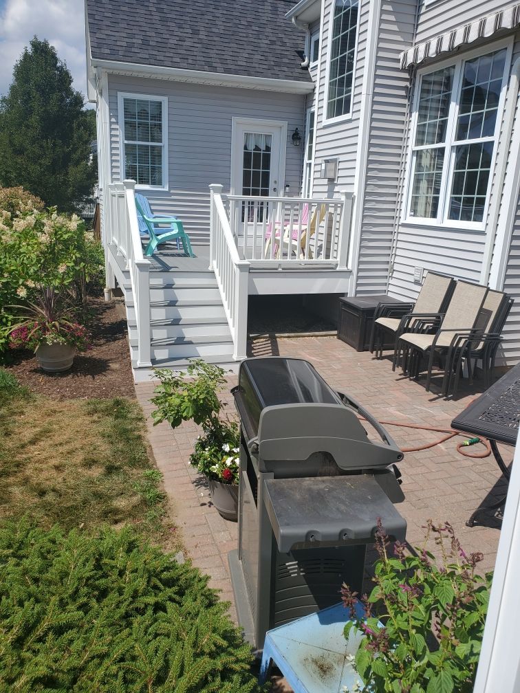 Backyard with a gray house, deck, and brick patio. Grill is on the patio.