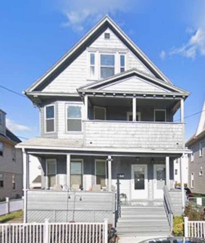 Gray multi-story house with front porches and white picket fence.