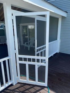 White screen door, open, on a porch with railing, leading to a home interior.