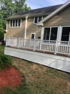 Tan house with a white deck and railings, brown lawn, and red mulch.