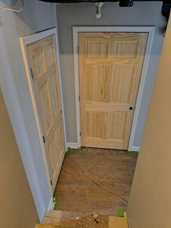 Two light wood panel doors with white trim in a basement hallway; gray and beige walls.