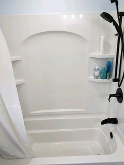 White bathtub with shower, built-in shelves, black fixtures, and a white shower curtain partially closed.