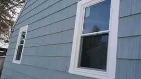 Two white-framed windows on a blue-sided house.