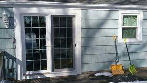 Sliding glass door and window on a light blue house exterior with snow shovels.