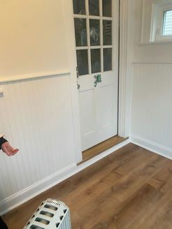 Interior with white door, wood floor, white paneled walls, and a small space heater.