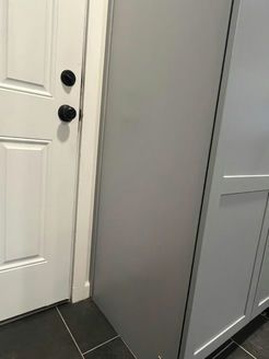 Gray cabinet next to a white door with black hardware, on a dark tiled floor.