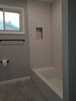 Bathroom with white subway tile shower, built-in shelf, gray walls, and a window.