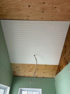 White paneled ceiling partially installed, wooden framing visible. Electrical wire hangs down. Green walls.