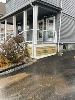 A house with a porch. The porch has a white railing, pillars, and a light-colored wooden base.