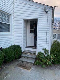 Exterior of white building with door, steps, and person partially visible. Shrubs on the left and right.