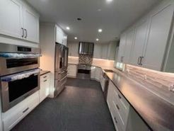 Modern kitchen with white cabinets, stainless steel appliances, dark floor, and under-cabinet lighting.