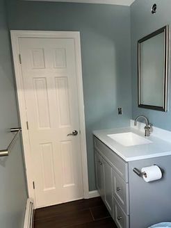 A bathroom with a gray vanity, a white sink, and a framed mirror; blue walls and a white door are present.