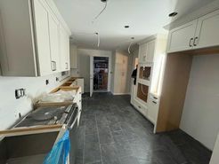 Kitchen under construction; white cabinets, gray floor, built-in oven, blue protective covering on stove.