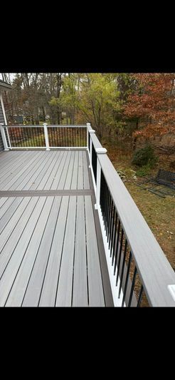 A wooden deck with gray boards and white railing overlooking a forest with colorful fall foliage.