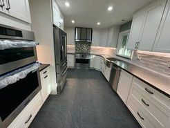 Modern kitchen with stainless steel appliances, white cabinets, gray countertops and flooring.