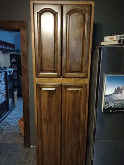Tall wooden pantry cabinet with four doors, dark stain, next to a refrigerator.