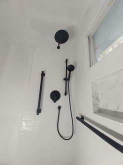 Black shower fixtures against white tiled wall. Includes overhead showerhead, handheld, and grab bars.