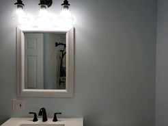 Bathroom with lit vanity lights above a mirror; faucet and sink visible, blue walls.