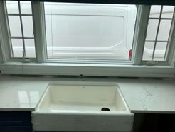 White farmhouse sink under a window, white countertop, and a glimpse of a white van outside.