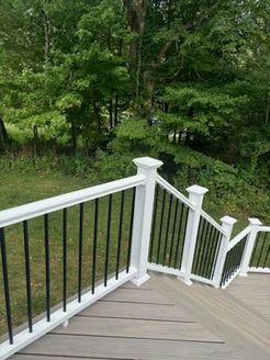 White railing with black spindles on a wooden deck overlooking a green lawn and trees.
