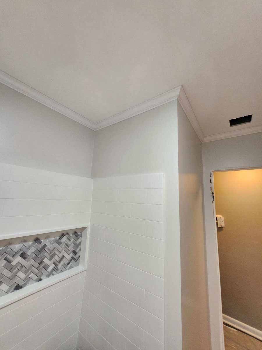 Corner of a bathroom with white walls, crown molding, and a tiled shower niche.