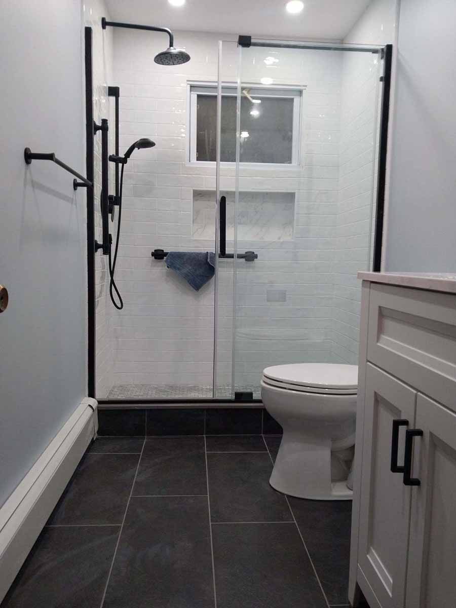 Small bathroom with black framed glass shower, white tile, black fixtures, and gray floor tiles.