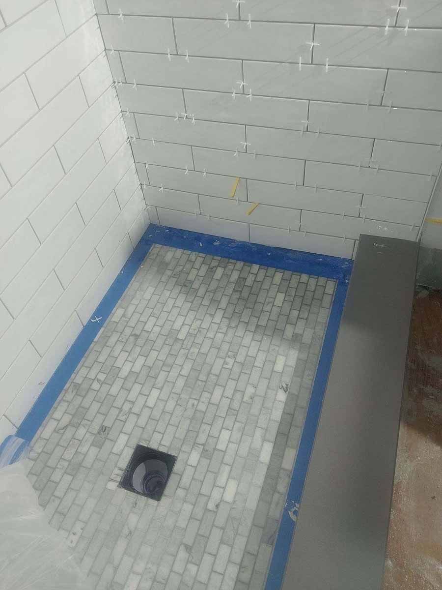 Shower stall with gray tile floor, white tiled walls, and blue tape around the edges.