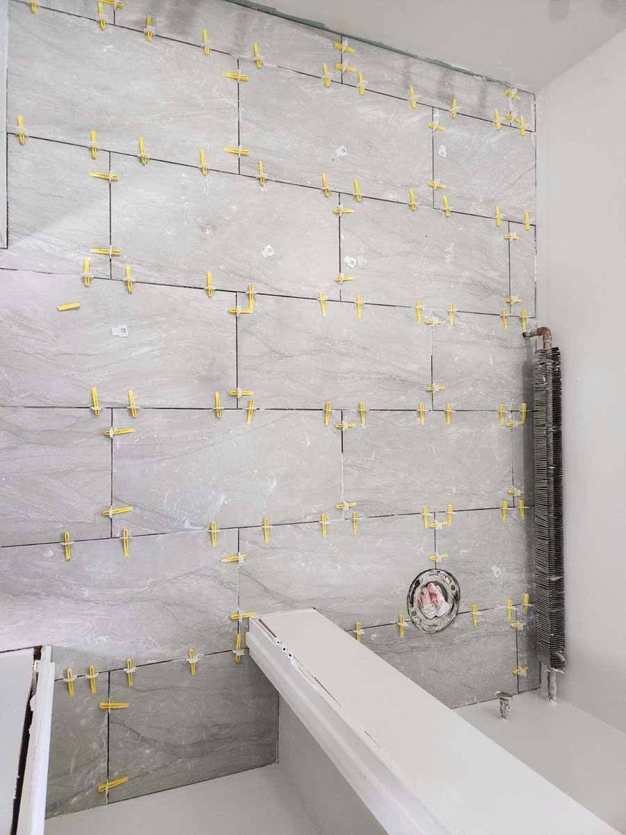 Gray tiled bathroom wall in progress, with yellow tile spacers.