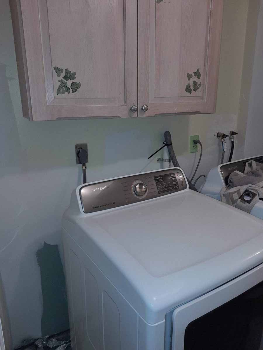 White washing machine in laundry room, under a cabinet with green leaf decorations.