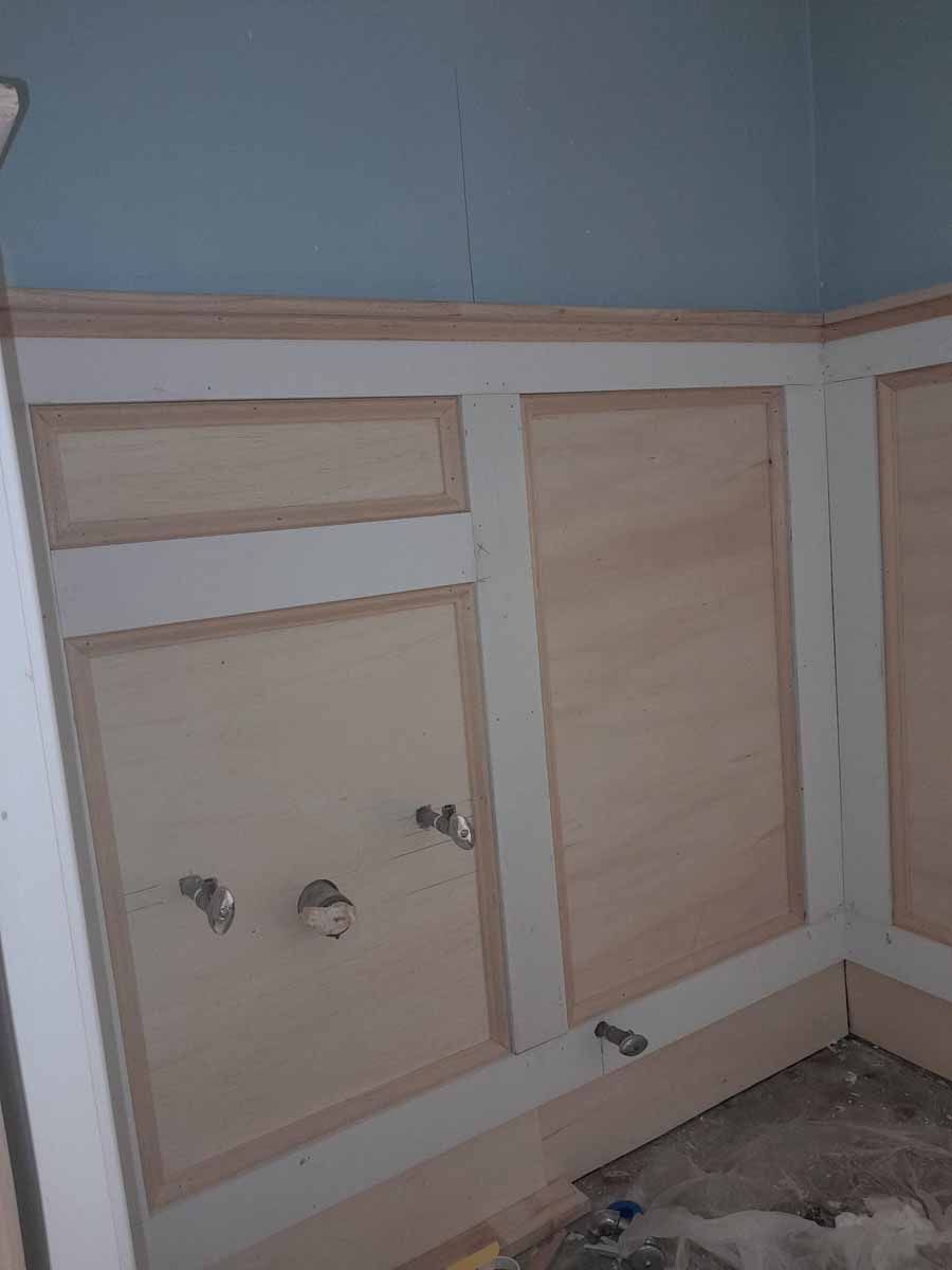 Wooden wainscoting on a wall with plumbing fixtures. The wall is blue above the paneling.