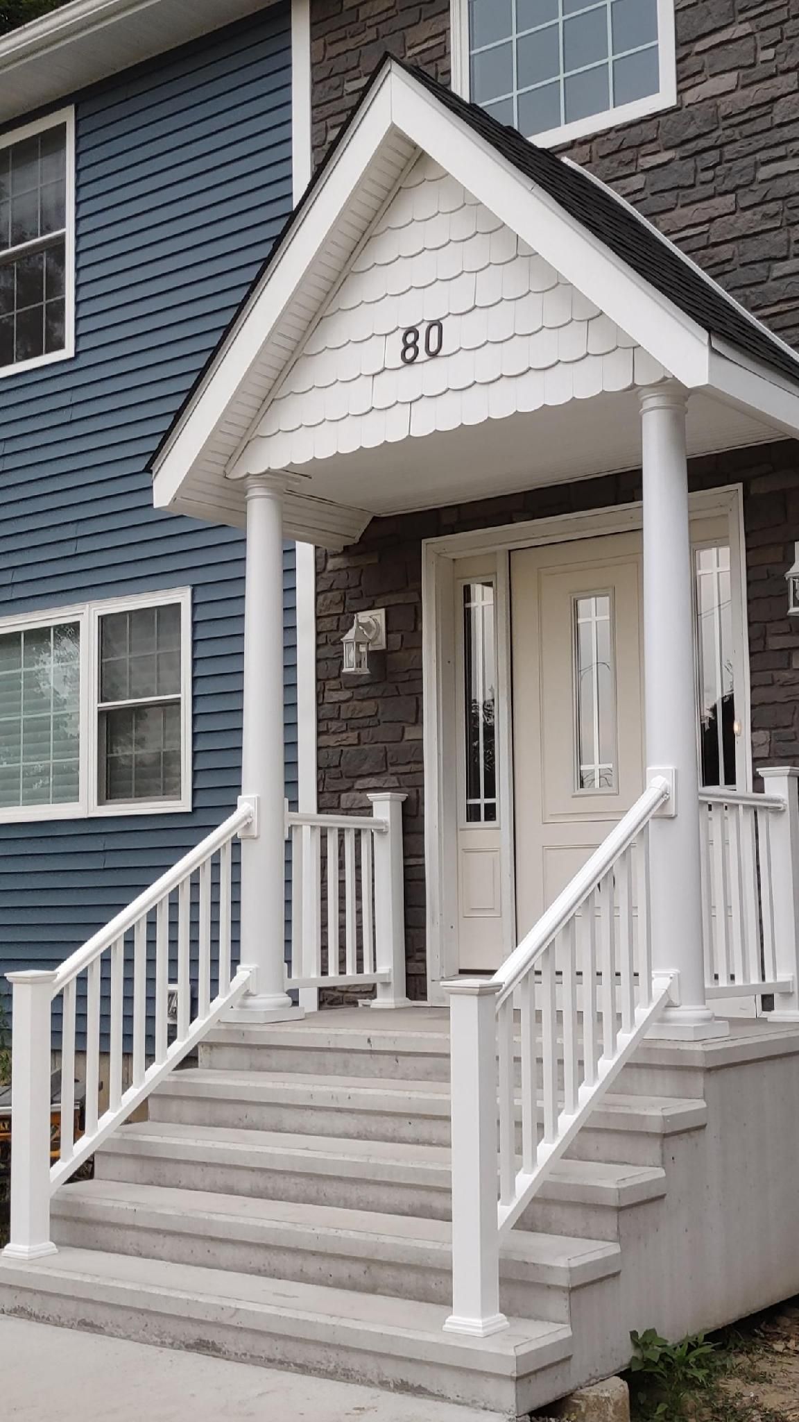 White porch with steps, columns, and railing leading to a house entrance. Blue and brown siding.