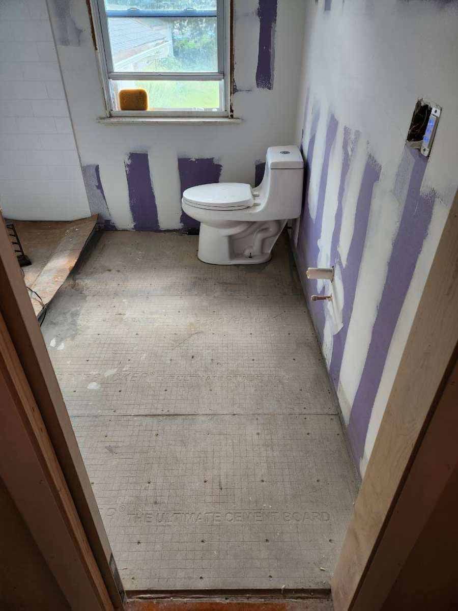 Bathroom under renovation; toilet installed, walls with drywall, unfinished floor, window visible.