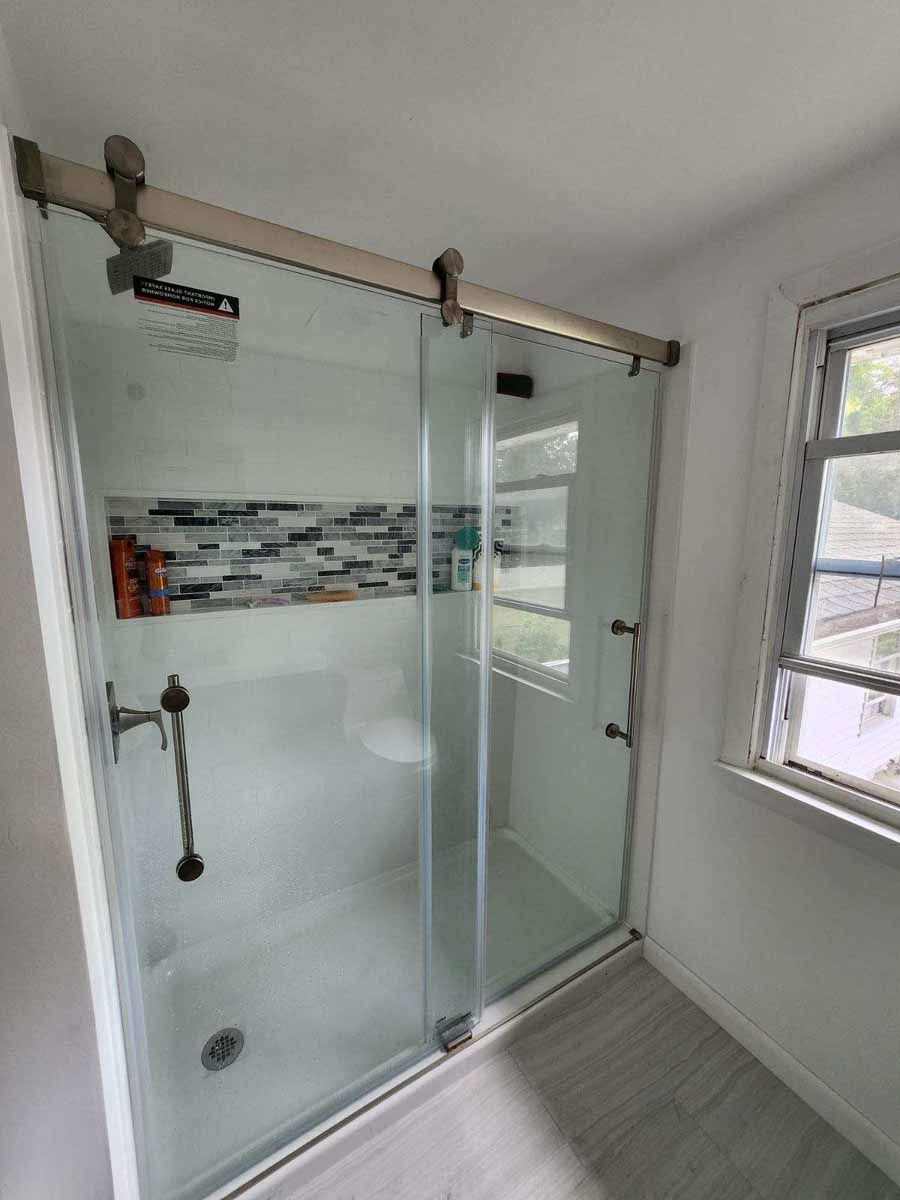Shower with sliding glass doors and a decorative tile strip. The hardware is brushed nickel. Next to a small window.