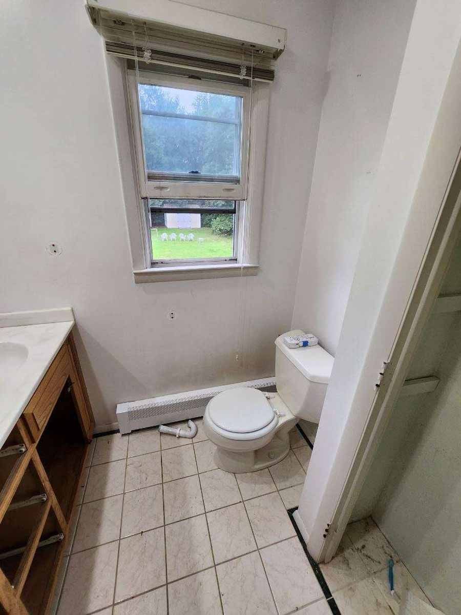 Bathroom interior with toilet, window, and vanity. Tiled floor, white walls.