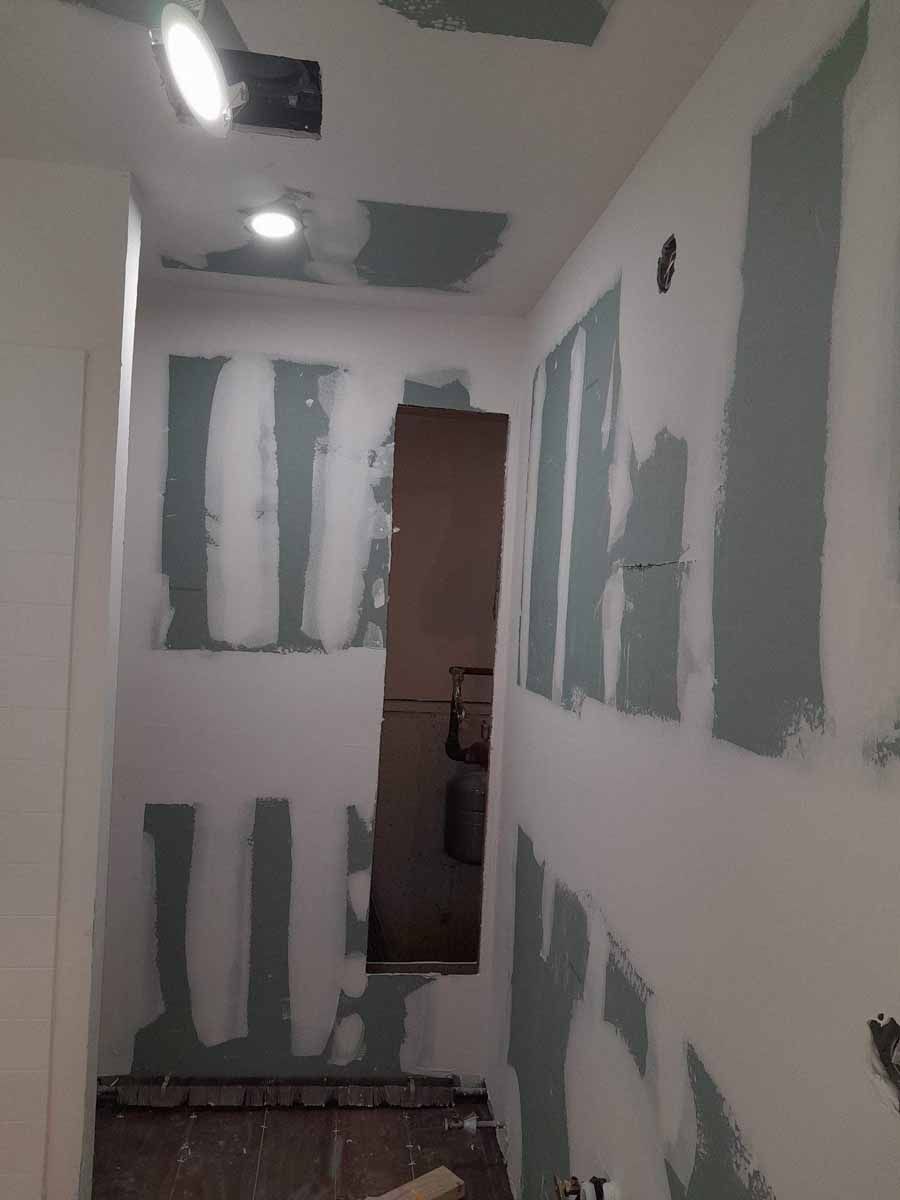 Hallway under construction; drywall partially installed. Gray mud on walls, recessed lights in ceiling.