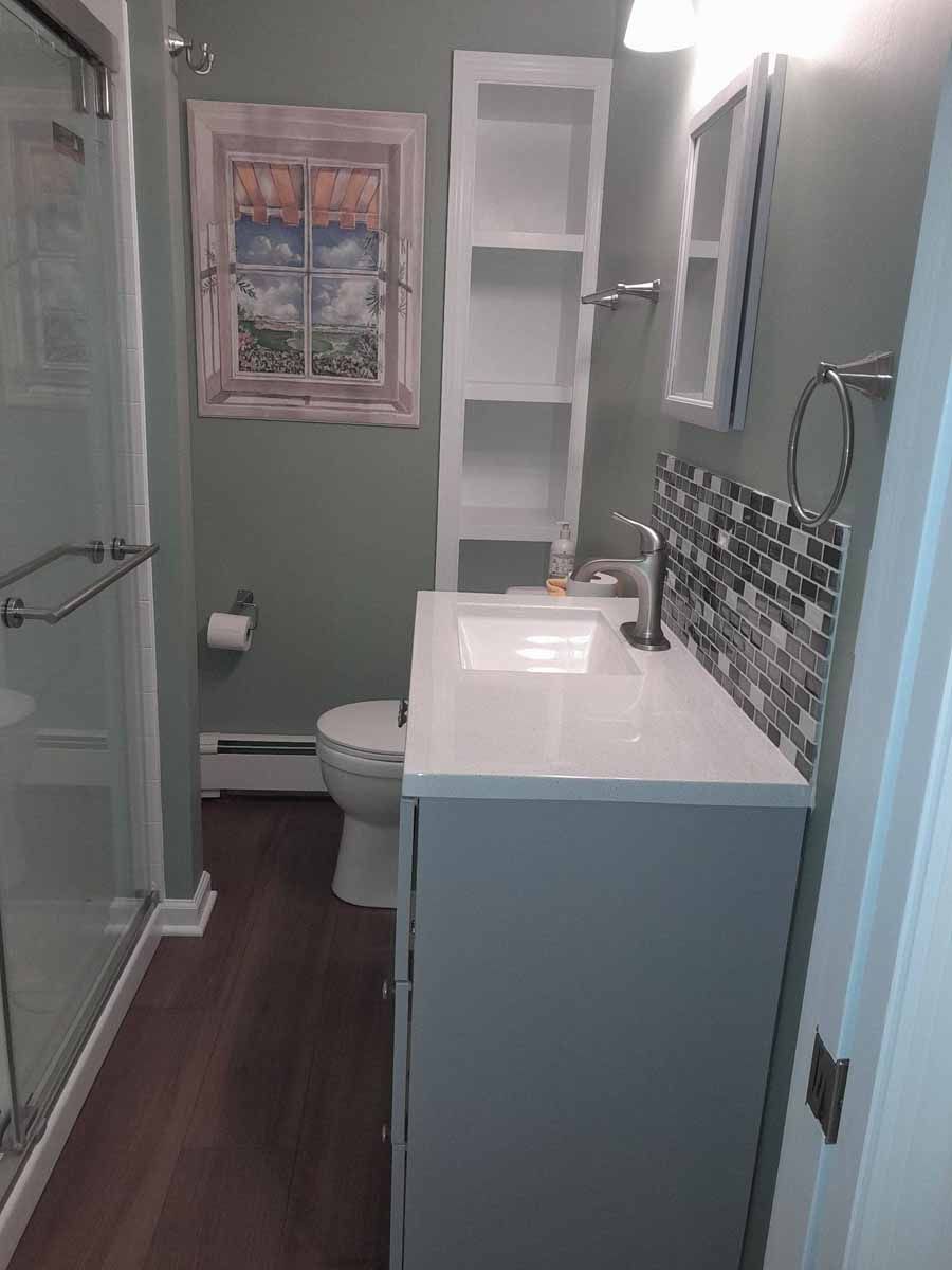 Small bathroom with a toilet, sink, and shower. Sage green walls and wood-look flooring.