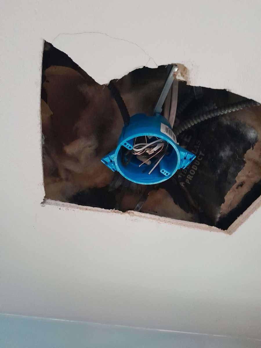 Blue electrical box with nails hangs from a hole in a white ceiling.