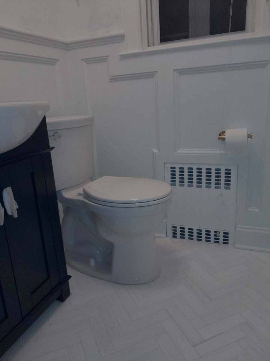 White bathroom with a toilet, dark cabinet, and radiator.