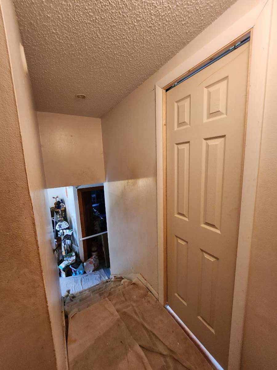 Hallway with a closed door on the right and an opening to a cluttered space on the left.