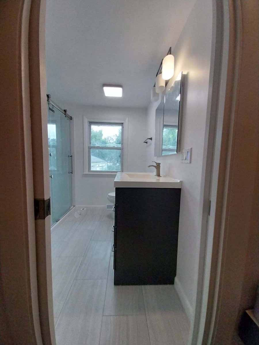 Bathroom with gray vanity, glass shower door, and window.
