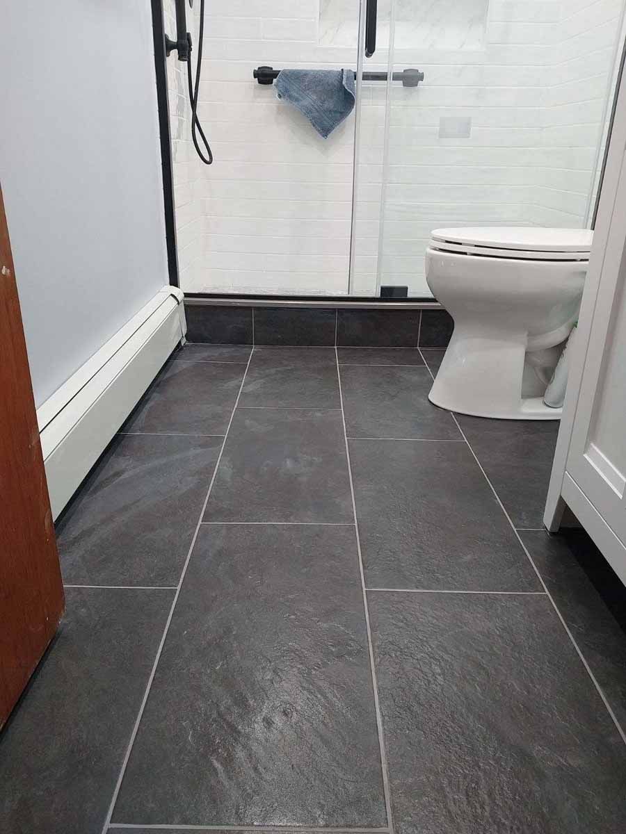Dark gray tiled bathroom floor with a toilet and shower visible.