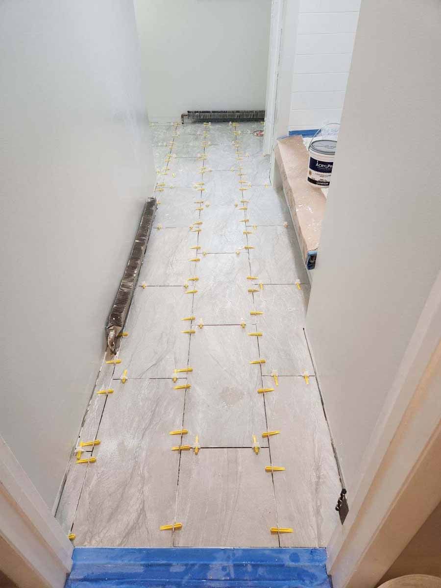 Hallway with new tile installation in progress; yellow tile spacers visible.