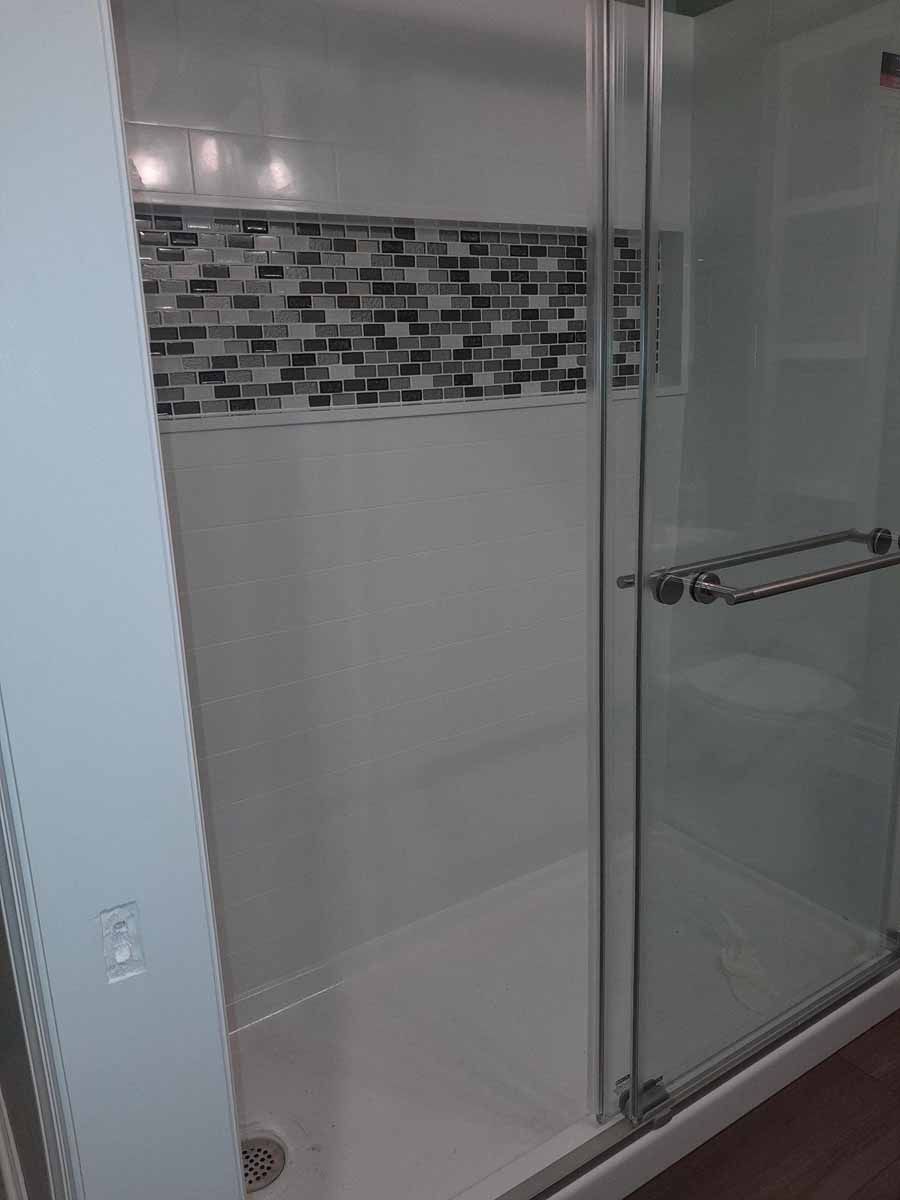 White shower with glass door and decorative tile accent.