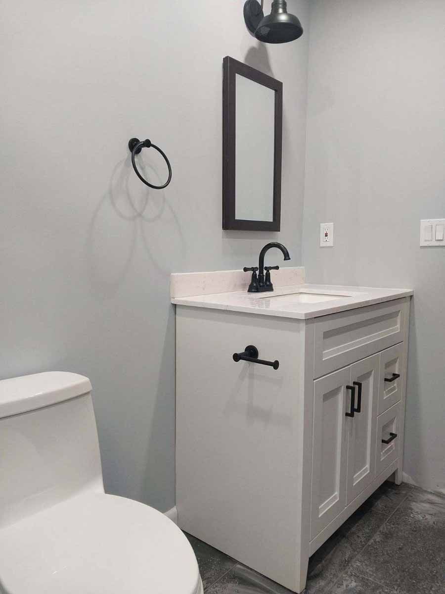 Small white bathroom with toilet, vanity, mirror, and black fixtures.
